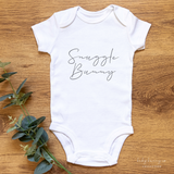 White onesie button close with Snuggle Bunny graphic on shirt with wooden background