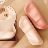 Reusable silicone bibs in cream and pink.