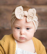 Baby wearing soft fit headband with bow in cream.