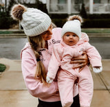 Mommy and baby wearing matching knitted pom pom hats in white.