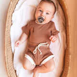 Baby wearing tee shirt and shorts set in brown with white trim.