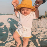 Baby wearing tee shirt and shorts set in white with mustard yellow trim.