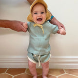 Baby wearing tee shirt and shorts set in sage green with white trim.