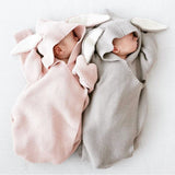 Two babies sleeping in knitted baby wraps with bunny ears hood in light pink and gray.