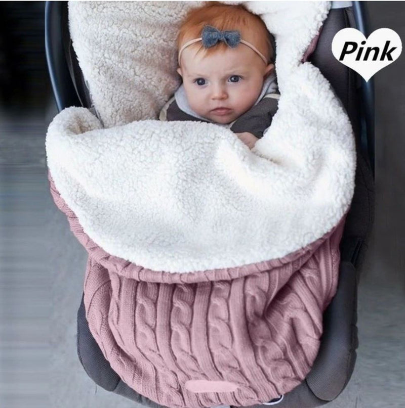 Baby in stroller laying on top of knit swaddle wrap in pink.  The swaddle is lined and for winter use. 