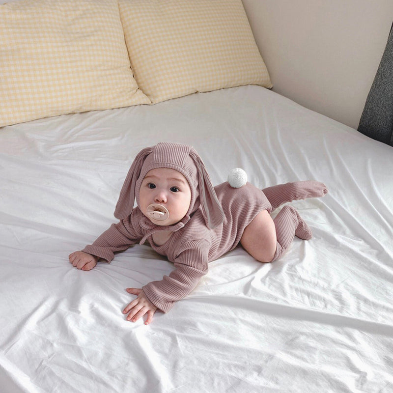 Baby on bed wearing matching 3 piece set in mauve.  Set includes hat with bunny ears, long sleeve onesie and socks.