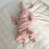 Baby on bed wearing matching 3 piece set in rose.  Set includes hat with bunny ears, long sleeve onesie and socks.
