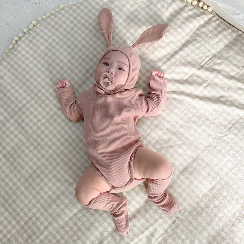 Baby on bed wearing matching 3 piece set in rose.  Set includes hat with bunny ears, long sleeve onesie and socks.