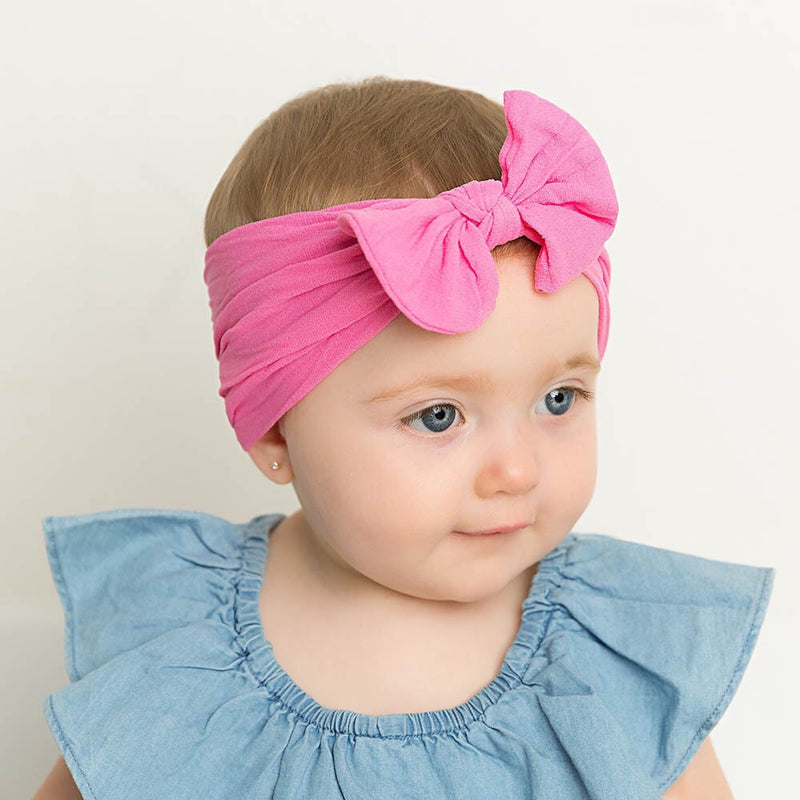 Baby wearing soft fit headband with bow in hot pink.