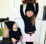 Girl and baby wearing matching knitted pom pom hat in black.
