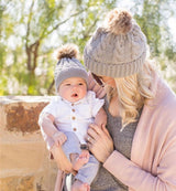 Mommy and baby wearing matching knitted pom pom hats in tan.