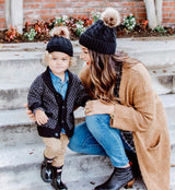 Mommy and baby wearing matching knitted pom pom hats in black.