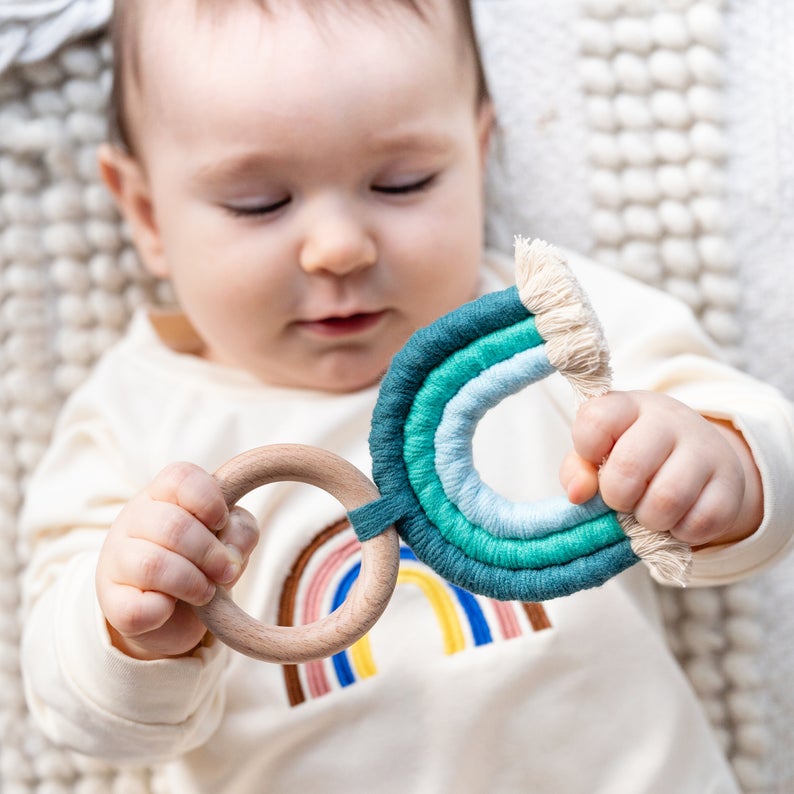Baby playing with handmade rainbow macrame wooden teether in blue.