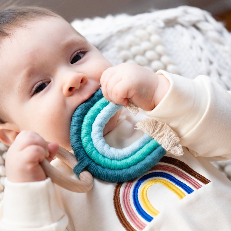 Baby playing with handmade rainbow macrame wooden teether in blue.